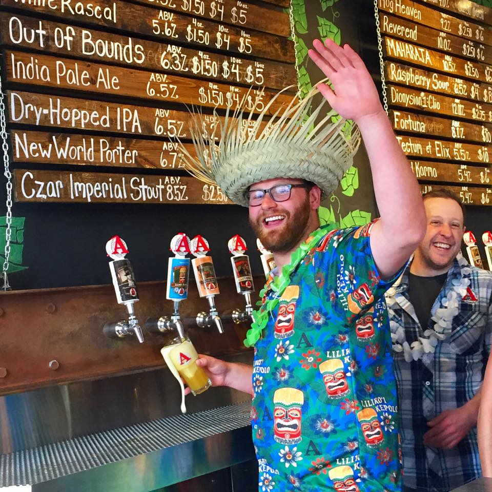 Walter Becker with hawaiian shirt and straw hat, pouring a beer, waving at the camera.