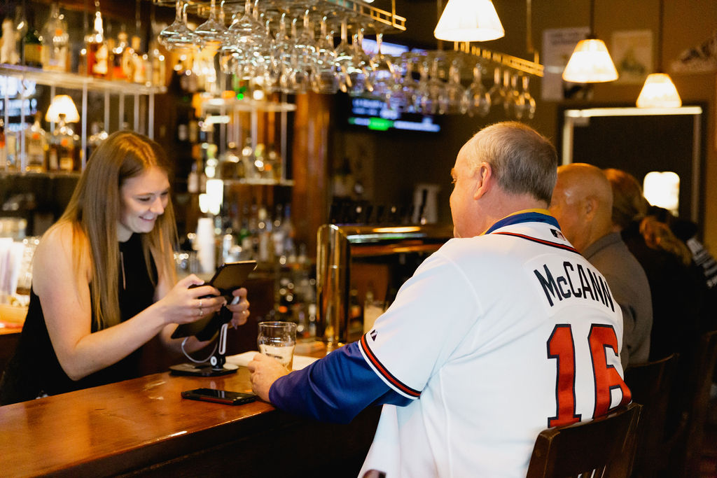 Bartender using mobile POS device with guests