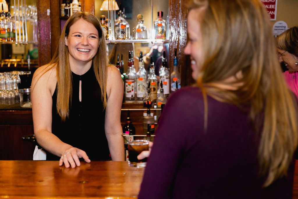 A bartender smiles at a guest after handing a drink over