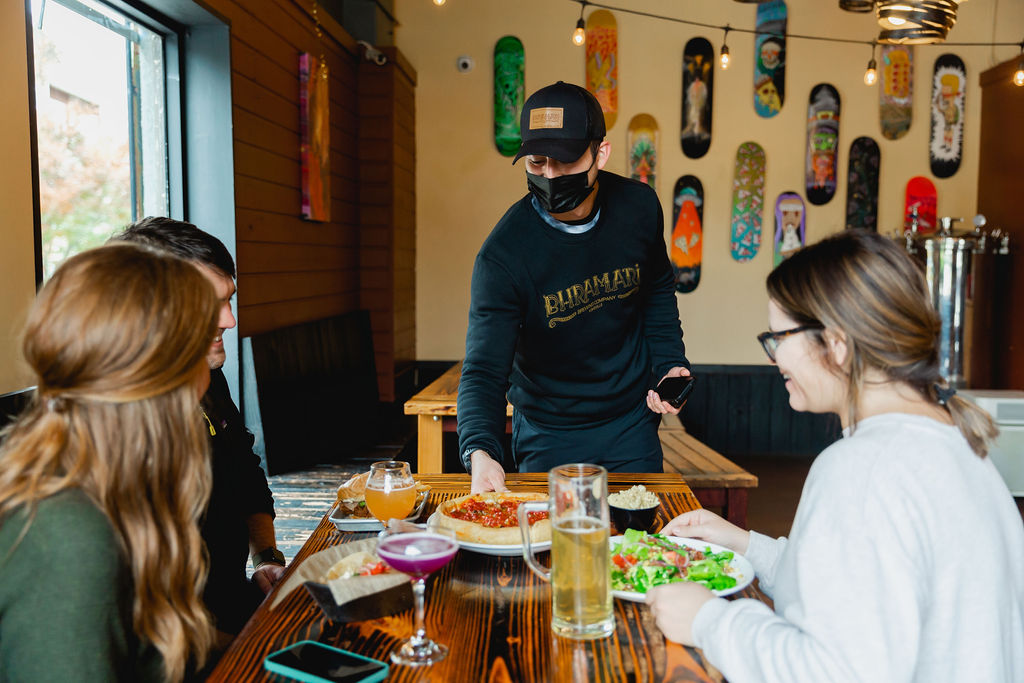 A server drops a fresh pizza at a table of guests