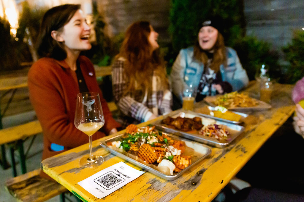 Friends laugh with full trays of food and drinks in front of them