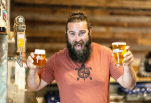 A person with a big smile holding up two beers 