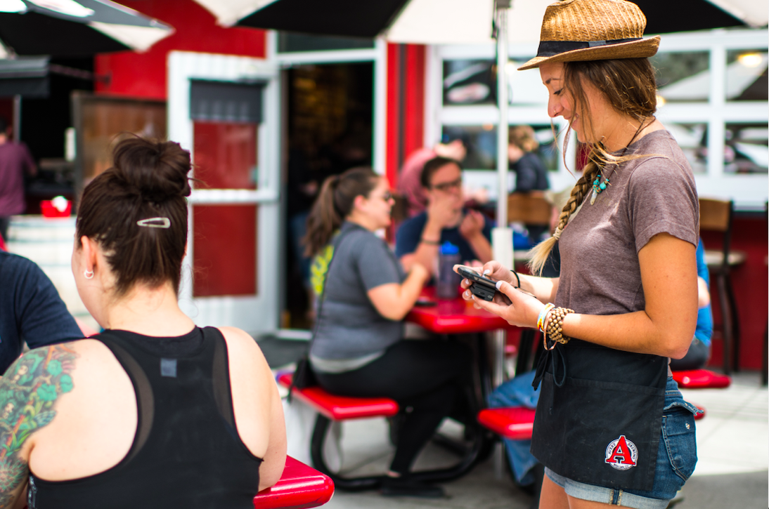 Server chatting with guests on patio with Arryved handheld in hands.