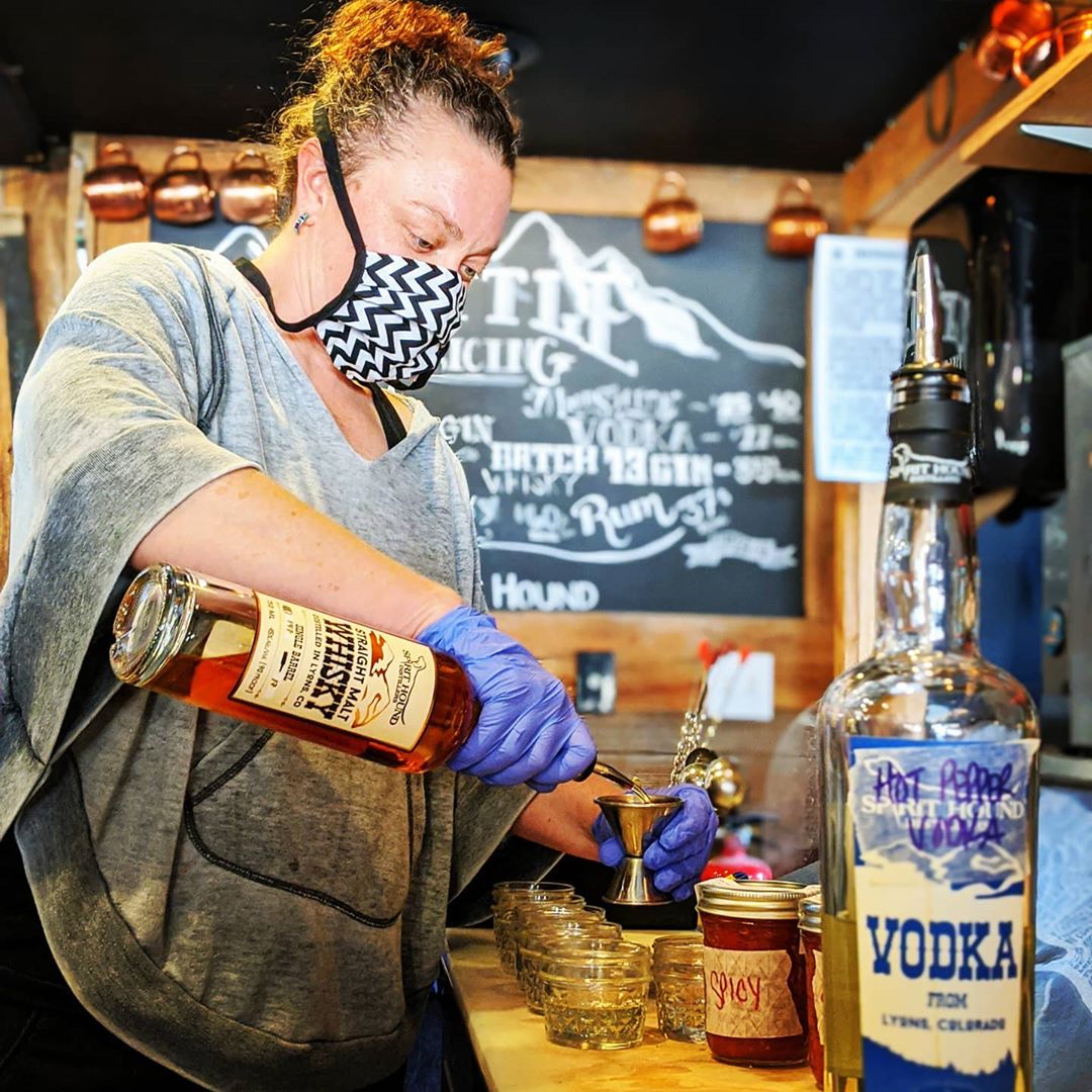 Bartender pouring whiskey into a shaker while wearing mask and gloves.