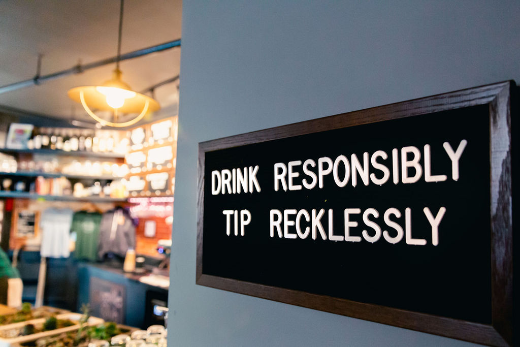 Decorative sign hanging in gift shop that says, "drink responsibly, tip recklessly".