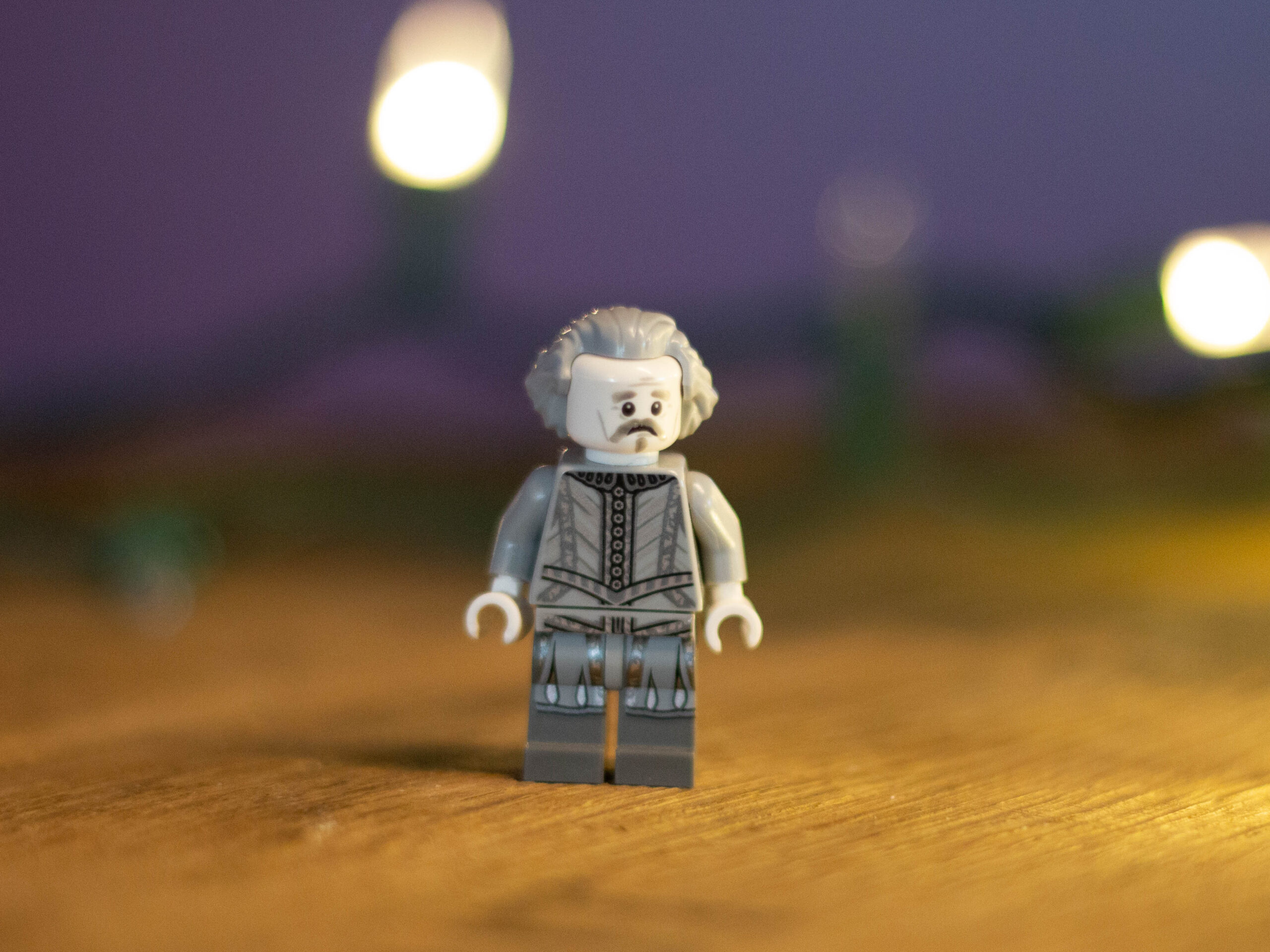 Older looking lego figure with grey hair standing on a wooden tables with a concerned look on its face