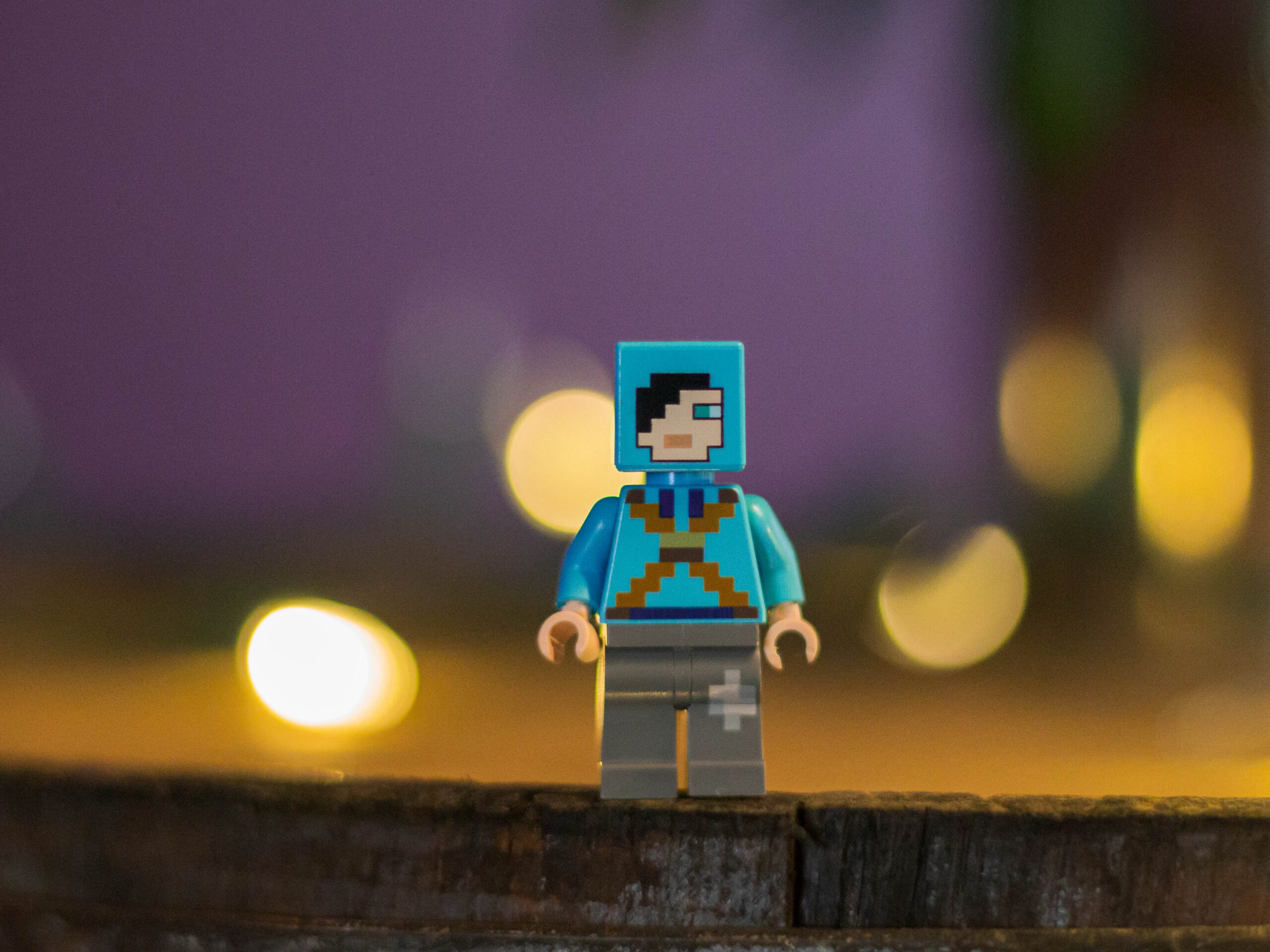 Blue lego figure with a block head standing on a piece of wood in front of lights