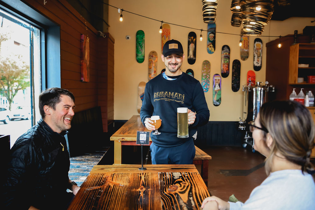 Server handing two beers to laughing guests