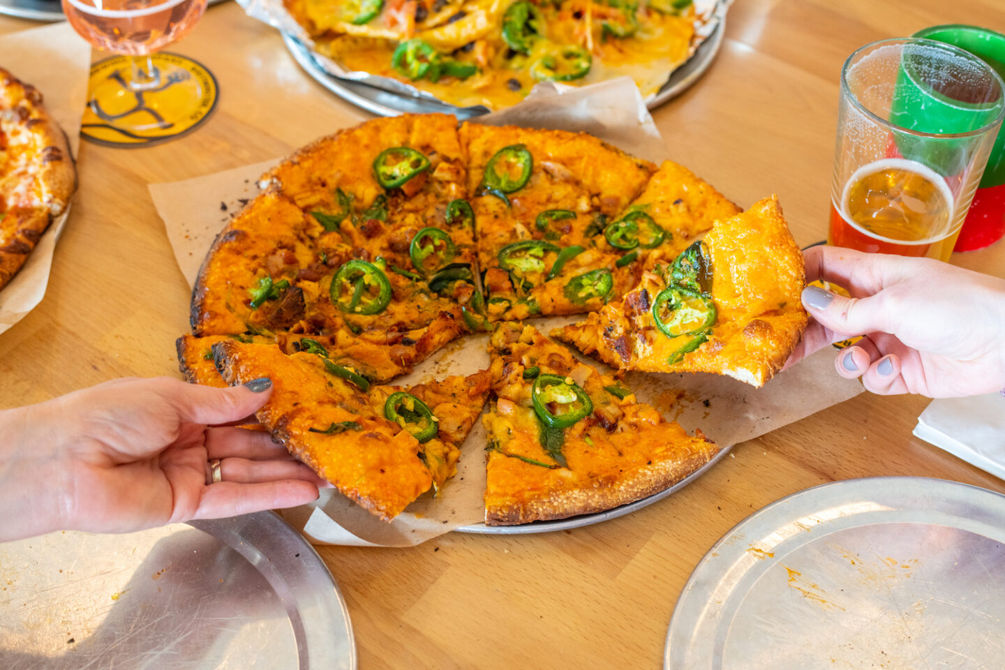 Two folks grabbing slices from a pizza with jalapeños and chicken.  